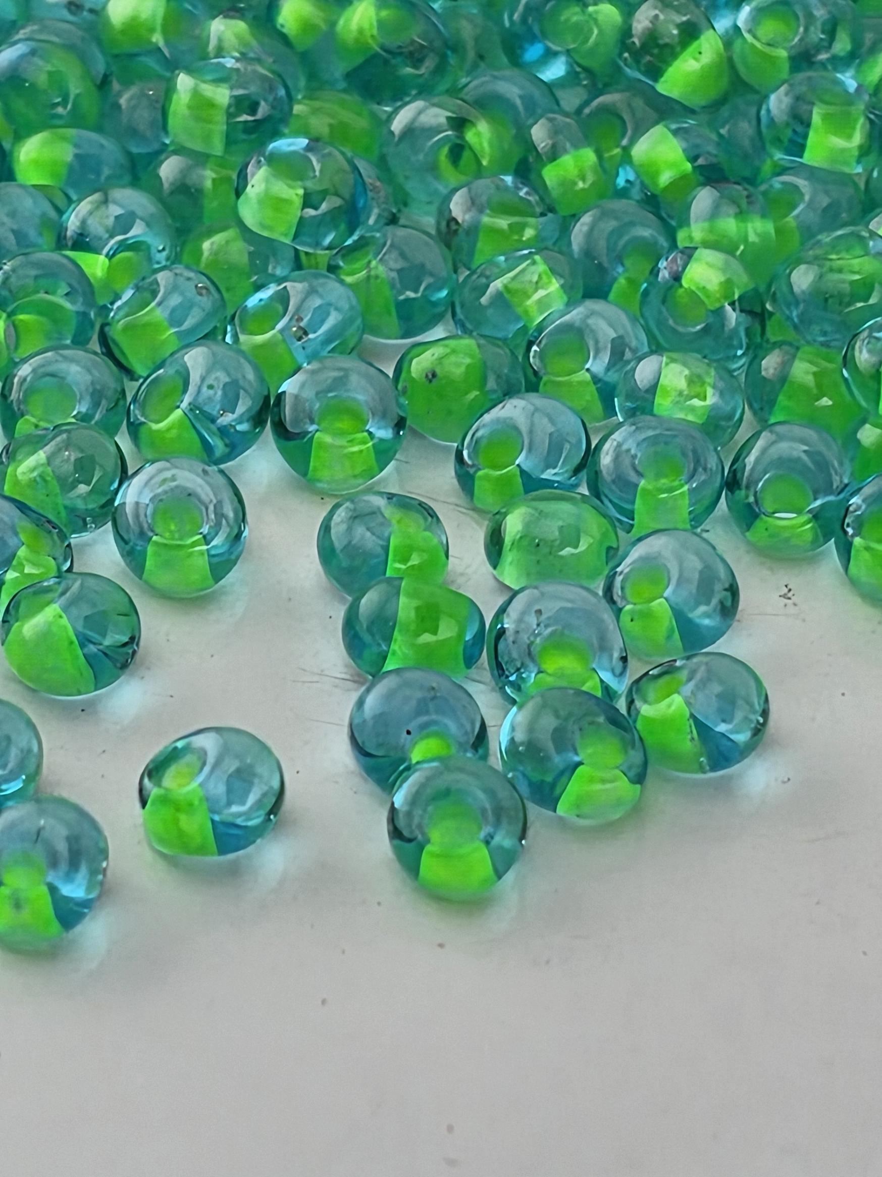a collection of small, clear glass beads in various shades of green and blue, scattered across a white surface.