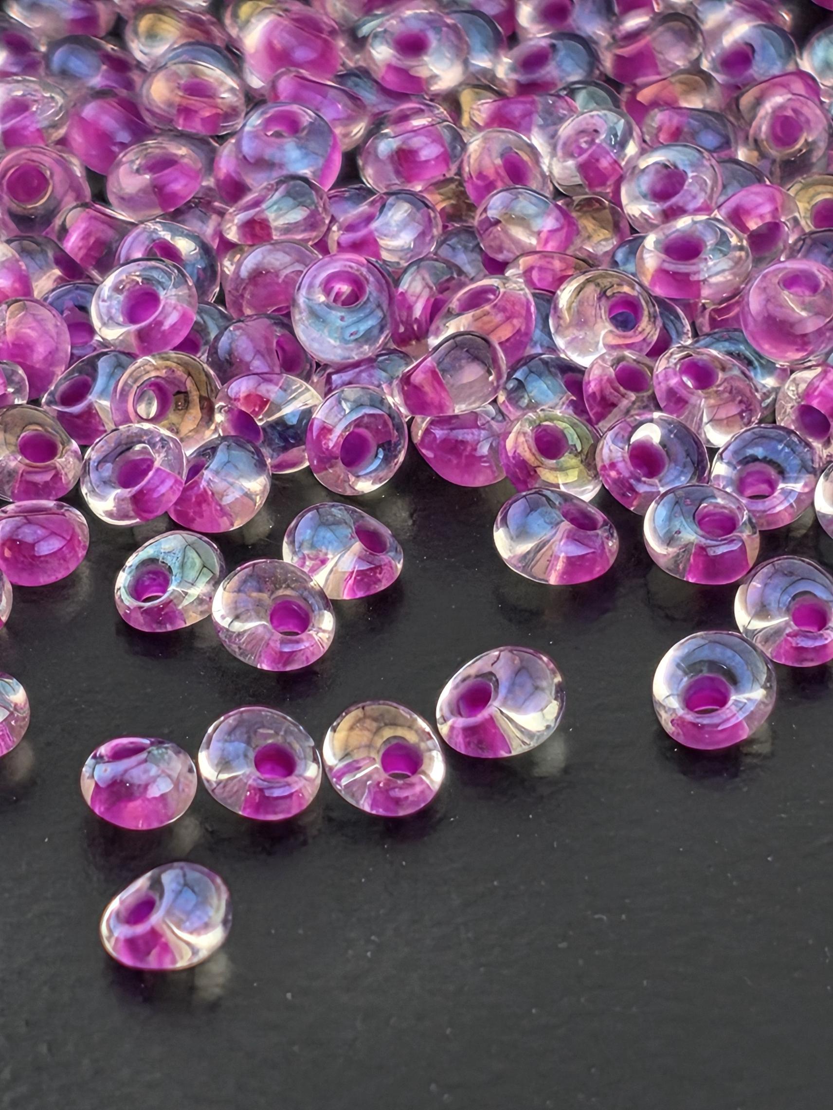a close-up view of numerous transparent beads in shades of pink and purple, scattered across a dark background.