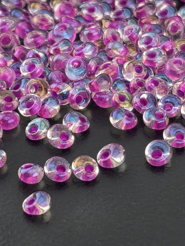a close-up view of numerous transparent beads in shades of pink and purple, scattered across a dark background.