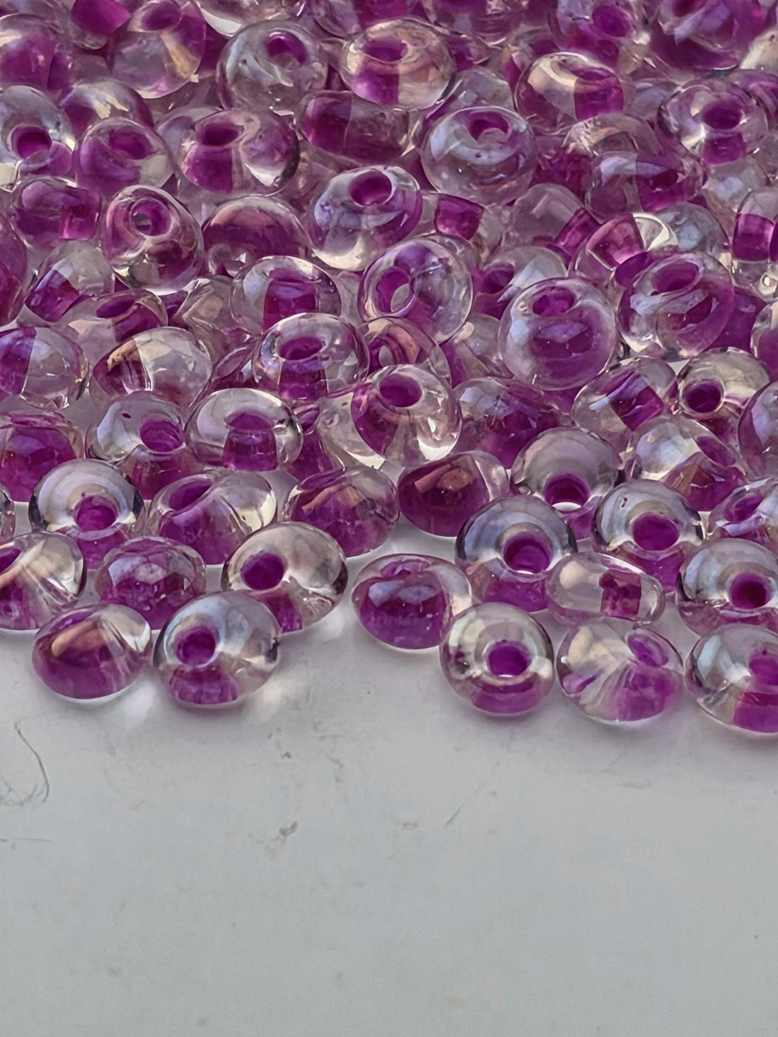 a close-up view of numerous transparent beads in shades of pink and purple, scattered across a dark background.