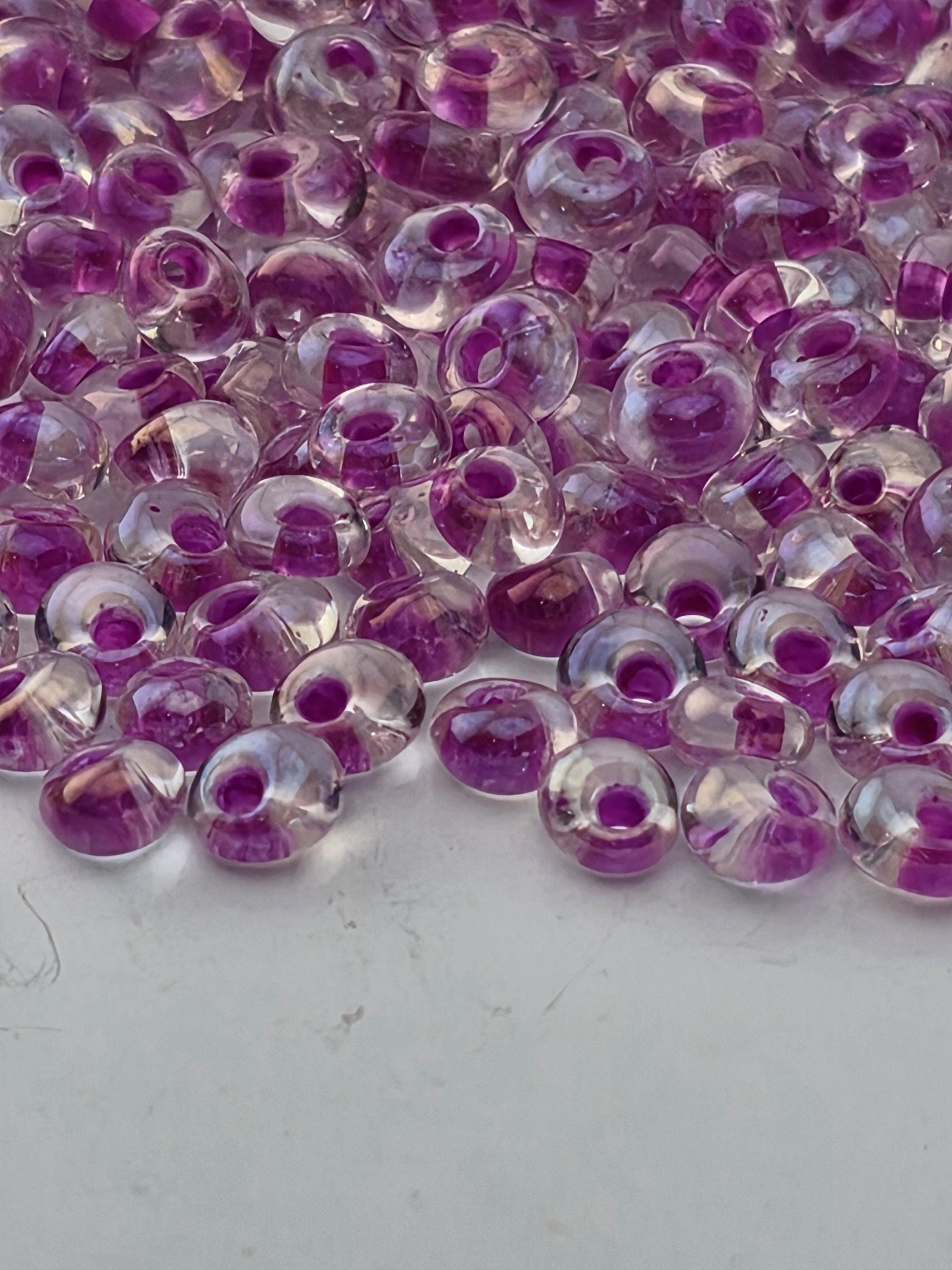 a close-up view of numerous clear beads with purple accents, scattered across a white surface.