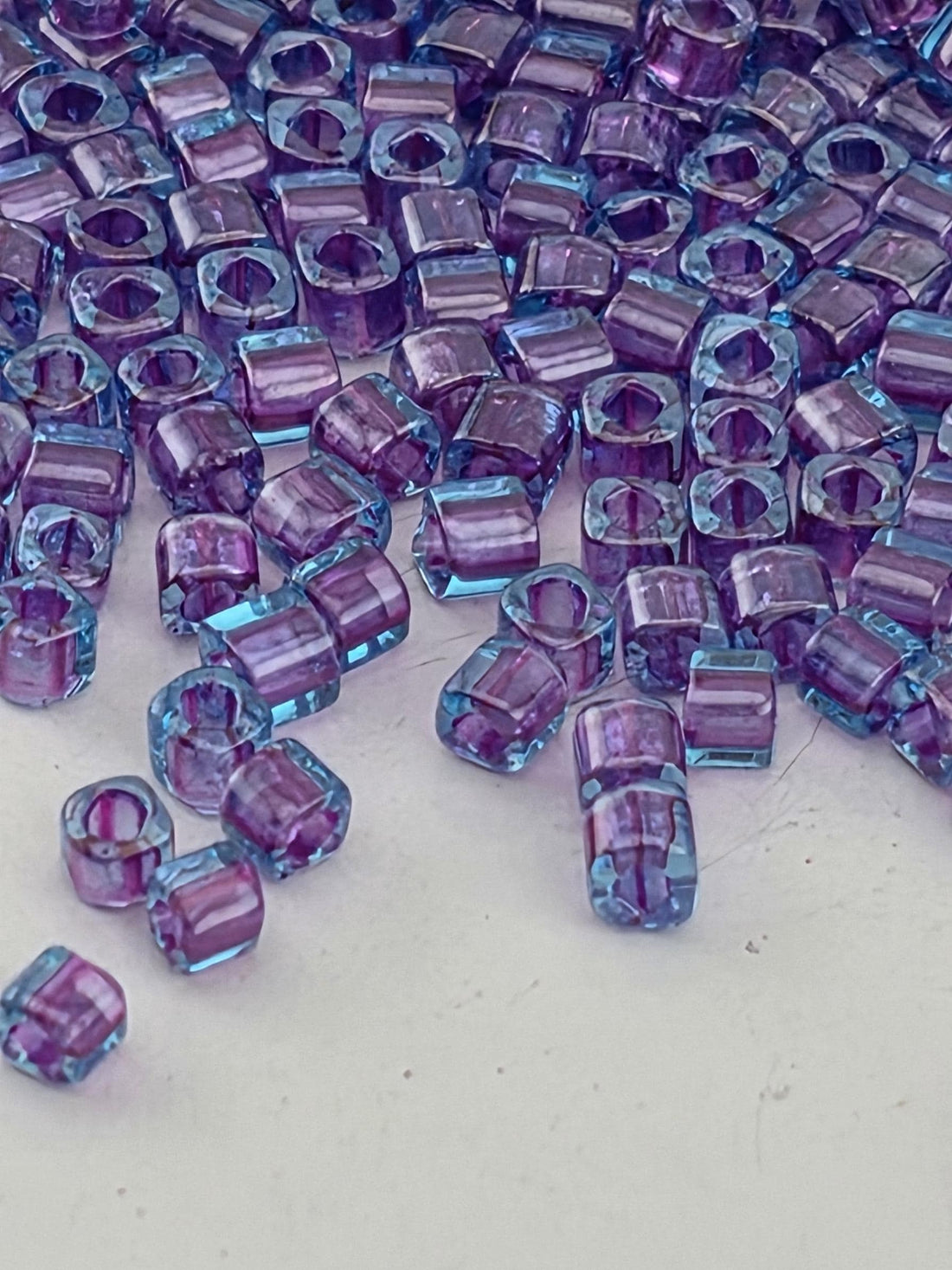 a close-up view of numerous small, clear beads in shades of purple and blue, scattered across a white surface.
