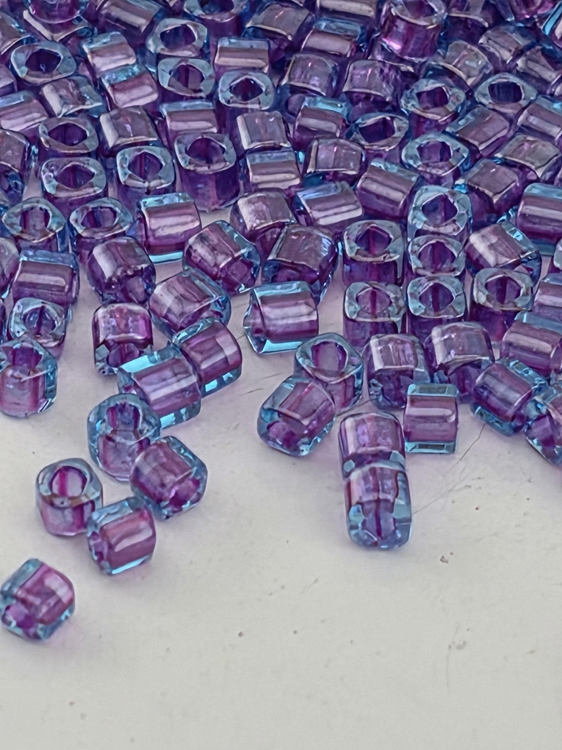 a close-up view of numerous small, clear beads in shades of purple and blue, scattered across a white surface.