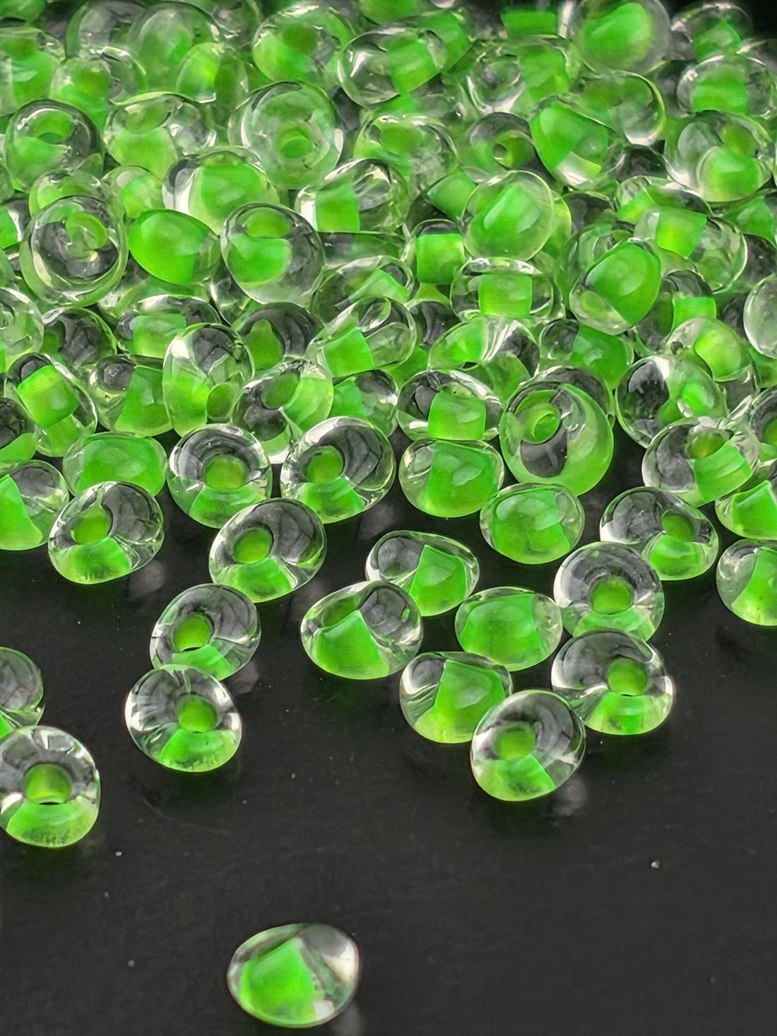a close-up view of numerous small, clear beads with a green tint, scattered across a dark background.