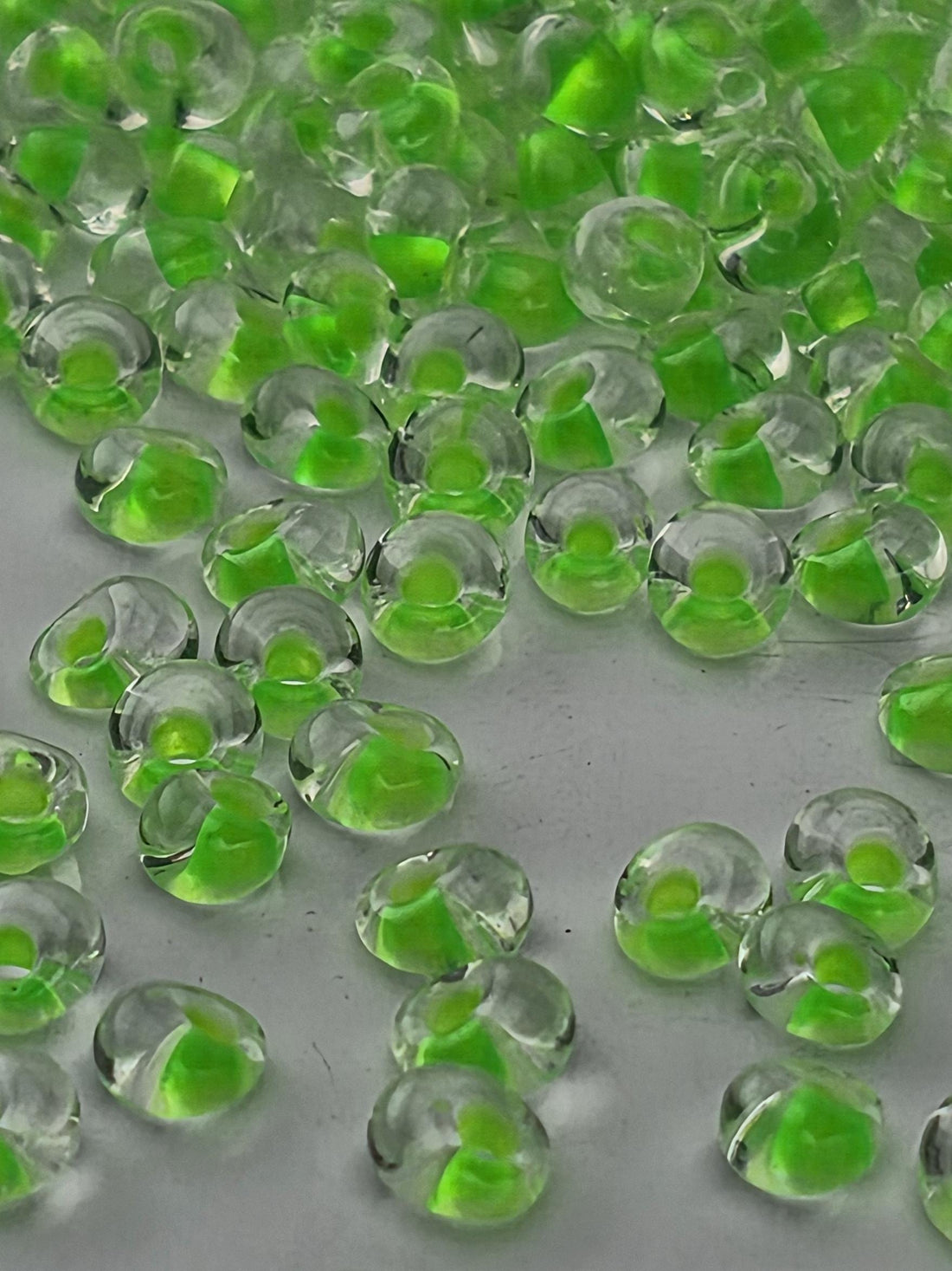a close-up view of numerous small, clear beads with a green tint, scattered across a dark background.