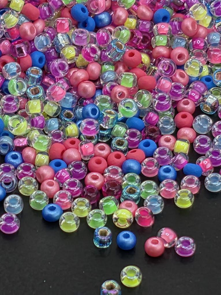 A colorful pile of multicolored plastic beads, including clear, blue, pink, and yellow beads, scattered on a dark surface.