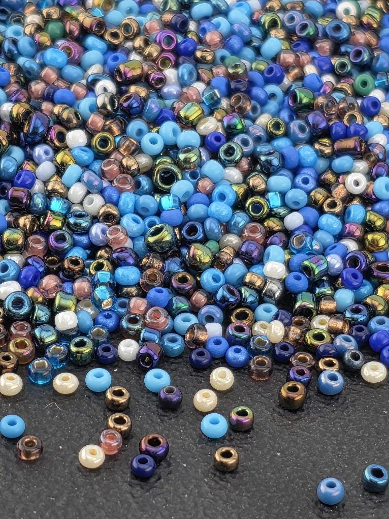 The image is a close-up of a pile of multicolored beads, including blue, purple, and gold beads, scattered on a dark surface.