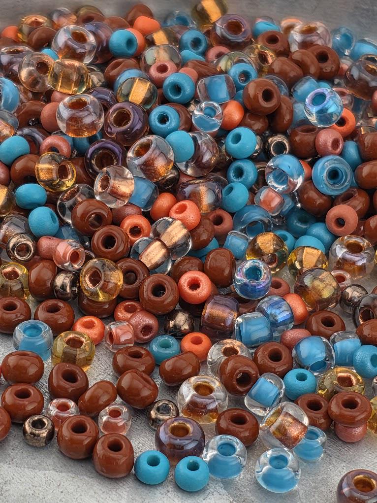 The image is a collection of various colored beads, including blue, brown, and clear beads, scattered on a surface.