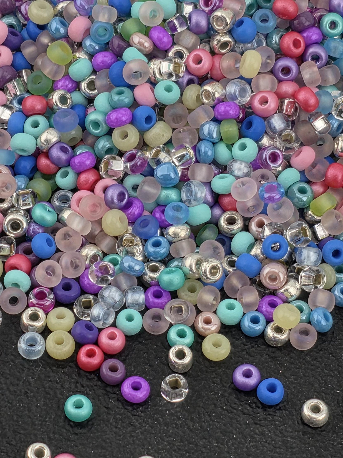 A colorful assortment of multicolored beads, including clear, transparent, and colored glass beads, scattered on a dark surface.