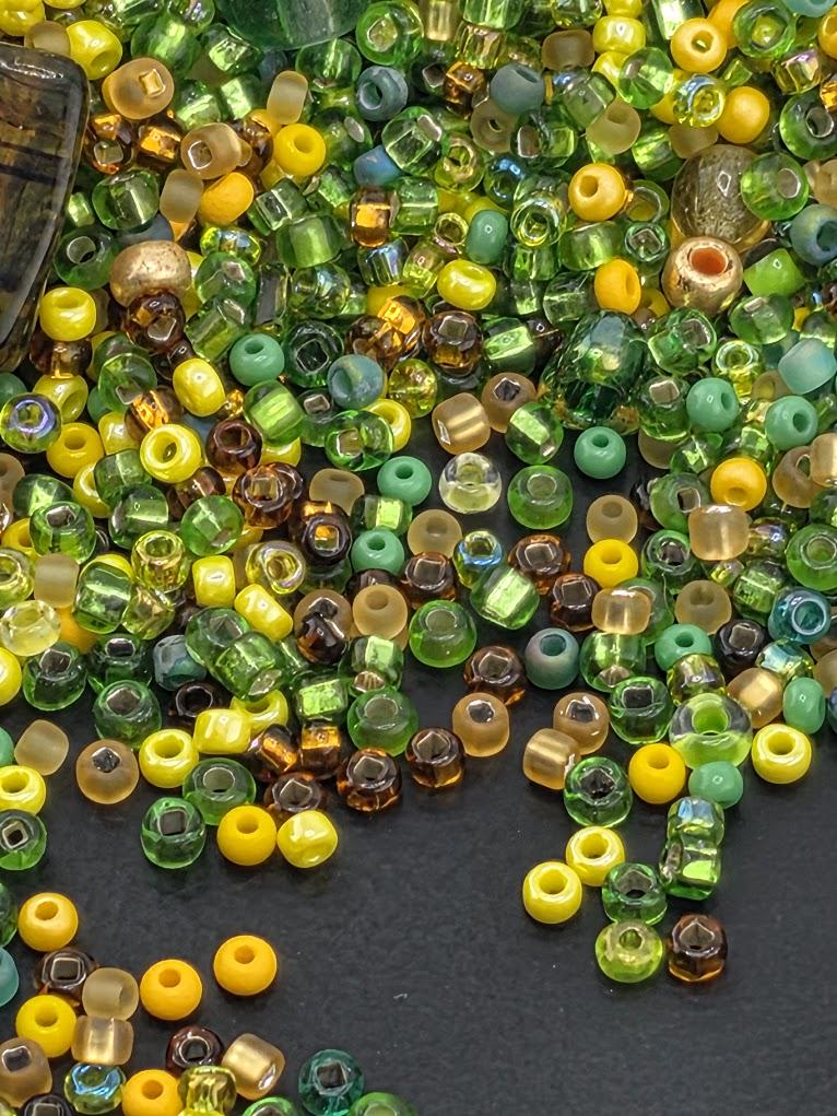 The image is a collection of various colored beads, including green, yellow, and brown, scattered on a dark surface.