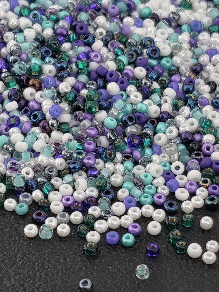 A pile of multicolored beads, including white, purple, green, and blue, scattered on a dark surface.