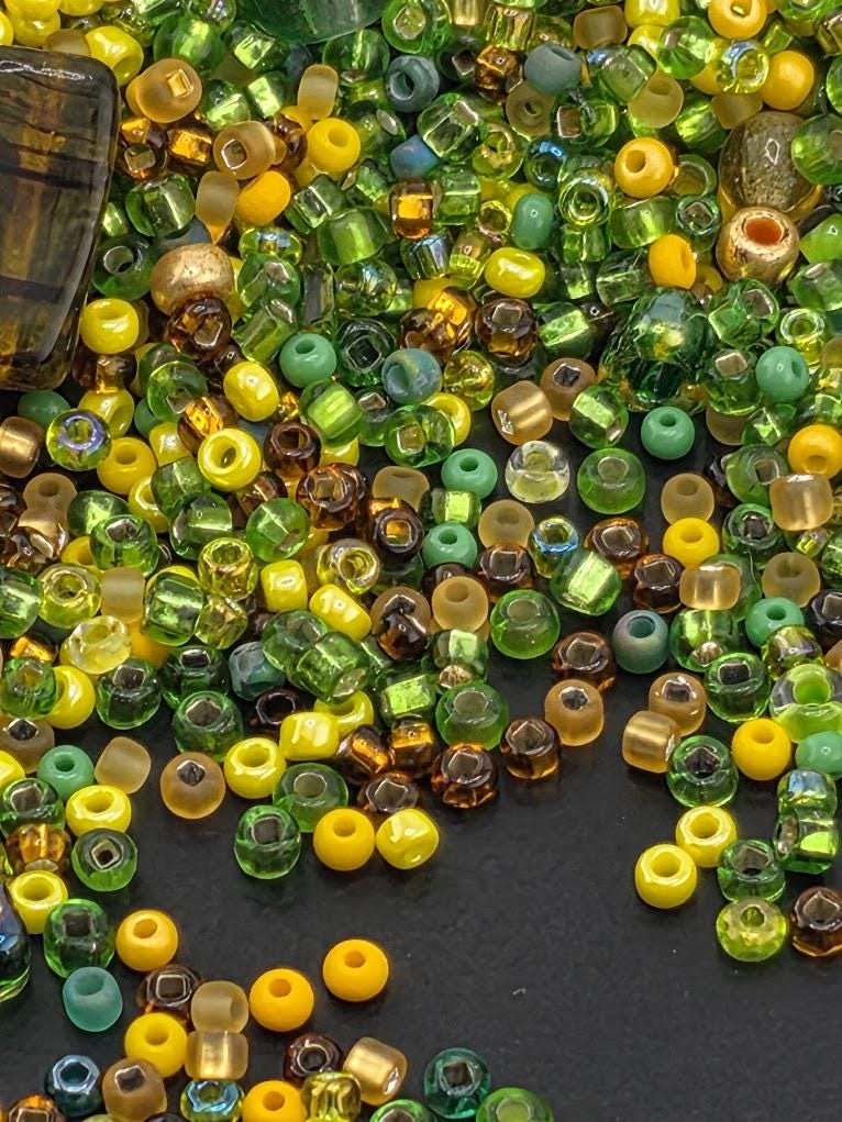 A colorful assortment of glass beads in various shapes and sizes, including green, yellow, and brown, scattered on a dark surface.