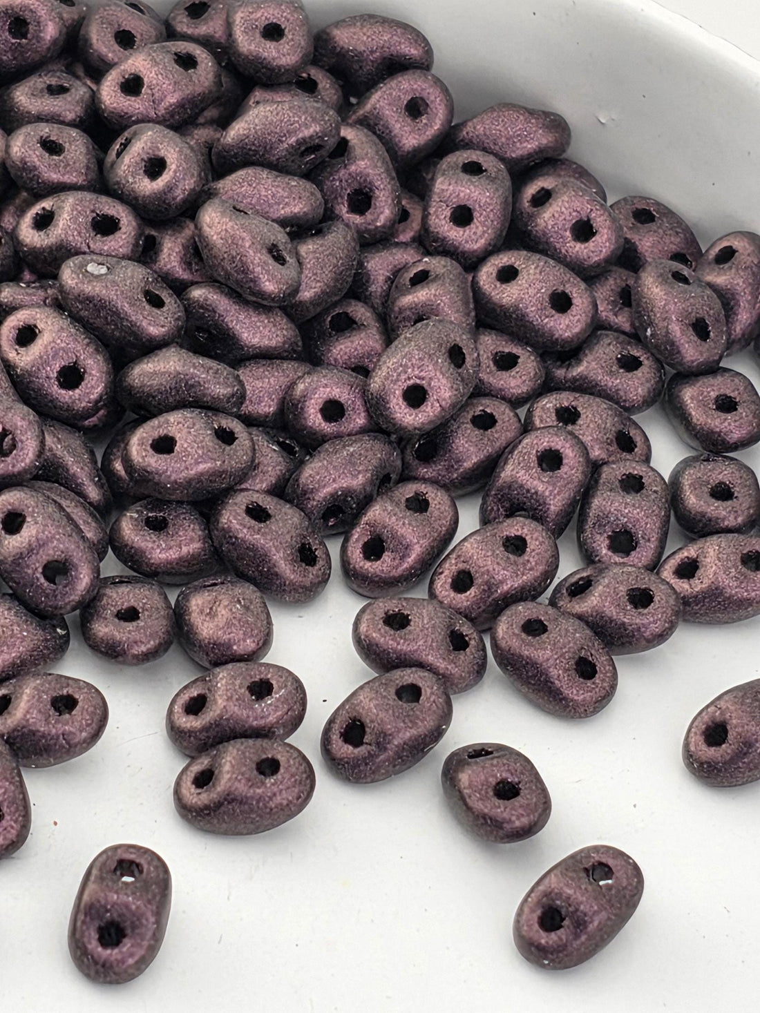 a close-up view of a pile of small, purple beads or beads with holes, scattered on a white surface.