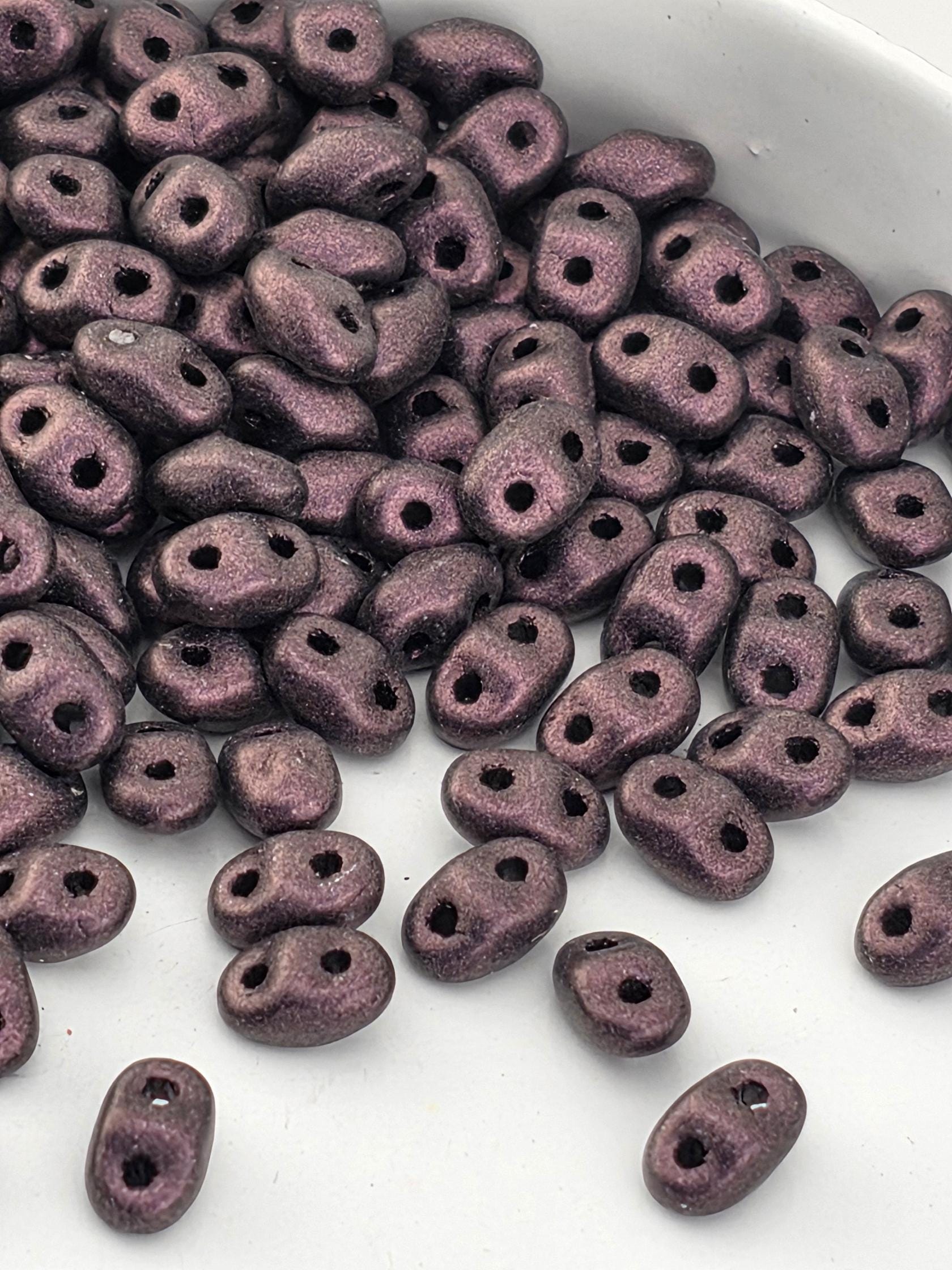 a close-up view of a pile of small, purple beads or beads with holes, scattered on a white surface.