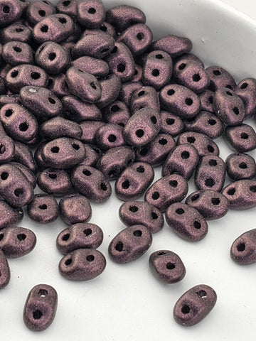 a close-up view of a pile of small, purple beads or beads with holes, scattered on a white surface.