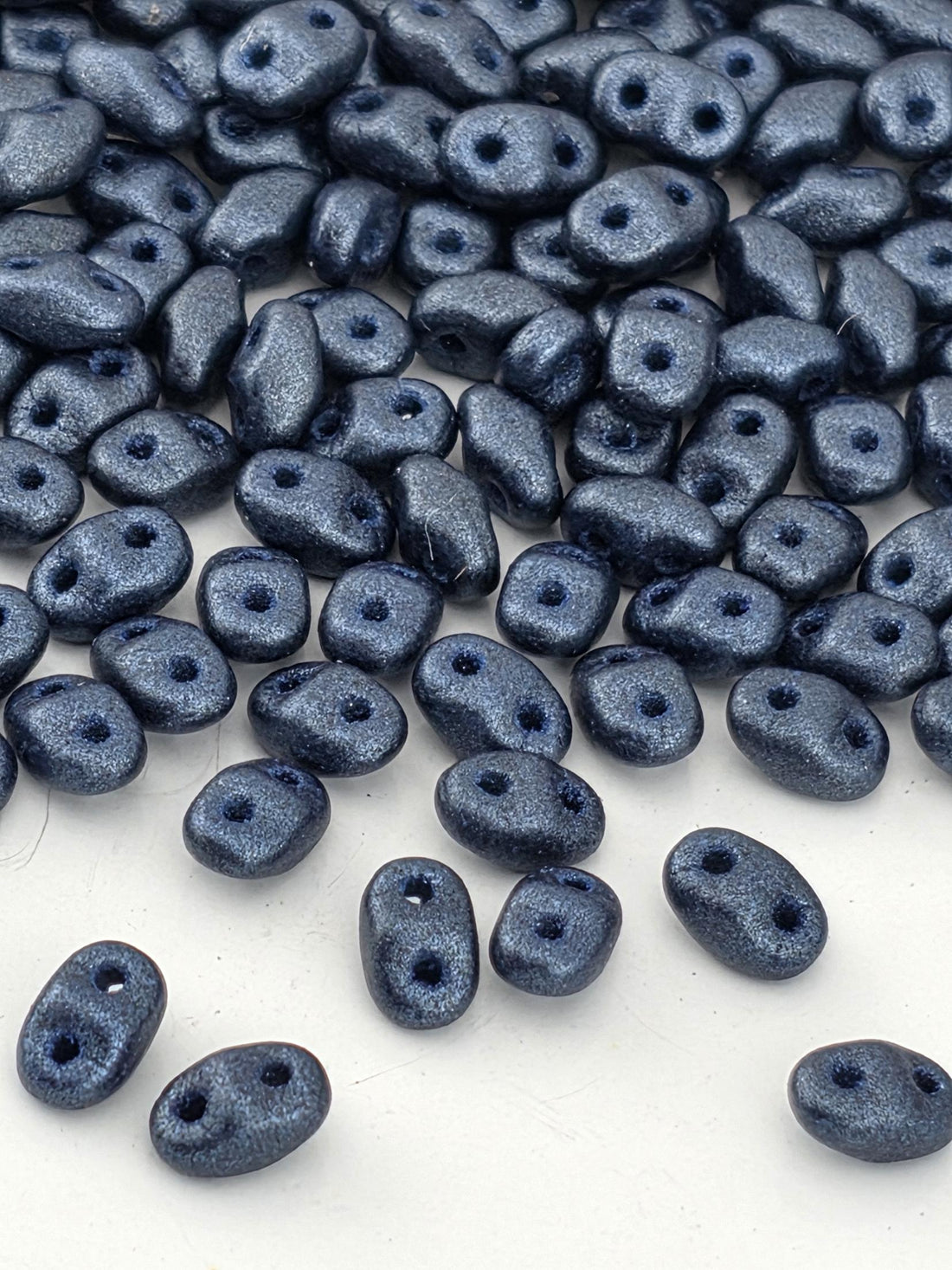 a collection of small, shiny blue beads scattered across a white background.