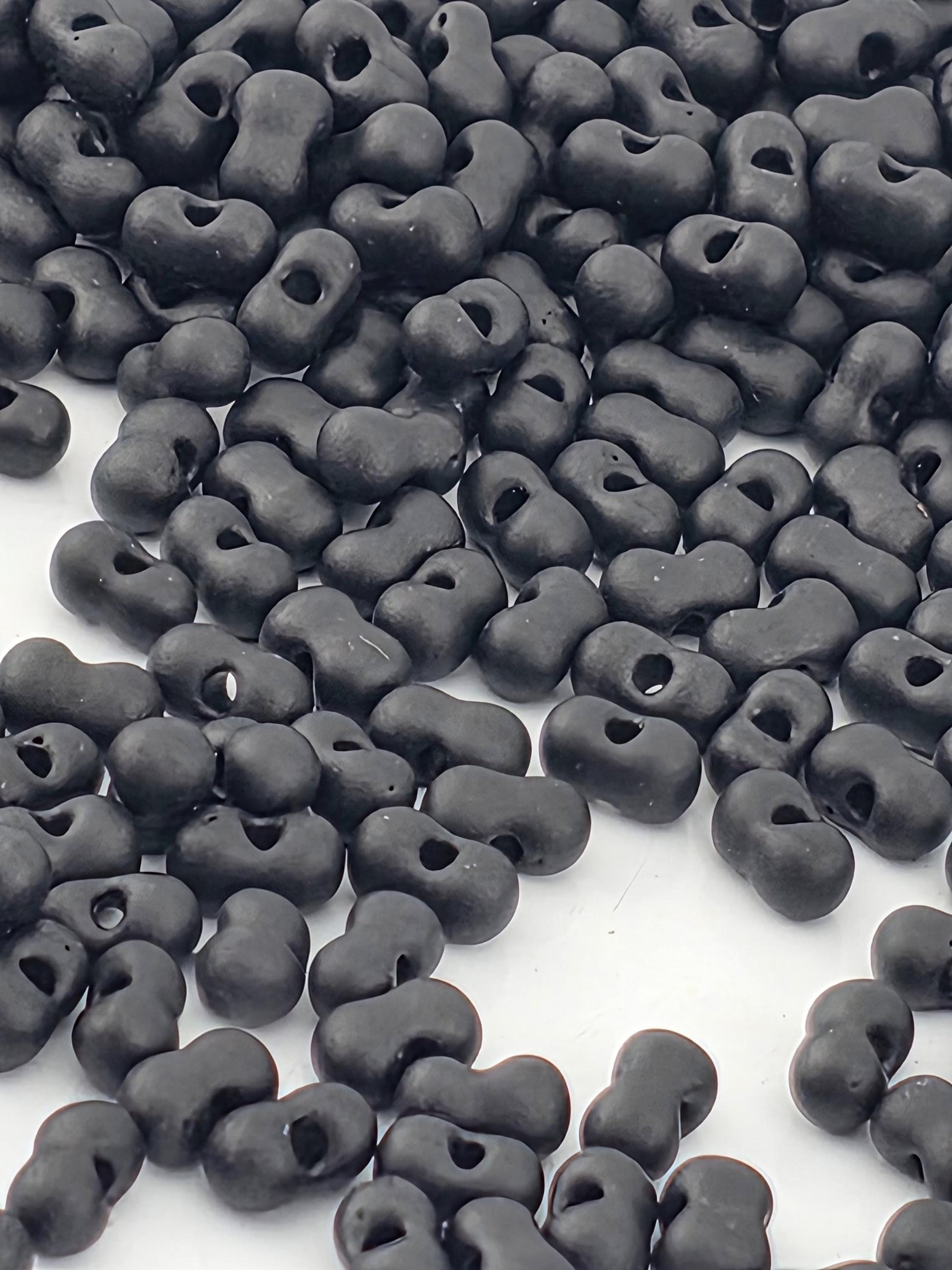a large pile of black beads or objects scattered on a white surface.