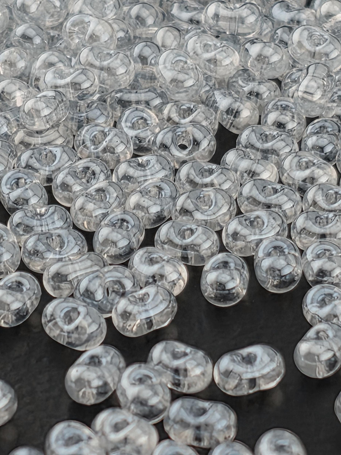 a collection of clear, oval-shaped glass beads scattered on a dark background.