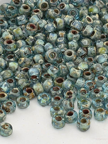 a large pile of small, blue glass beads scattered on a white surface.
