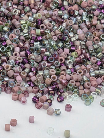 The image is a collection of various colored beads, including pink, purple, and green, scattered across a white surface.