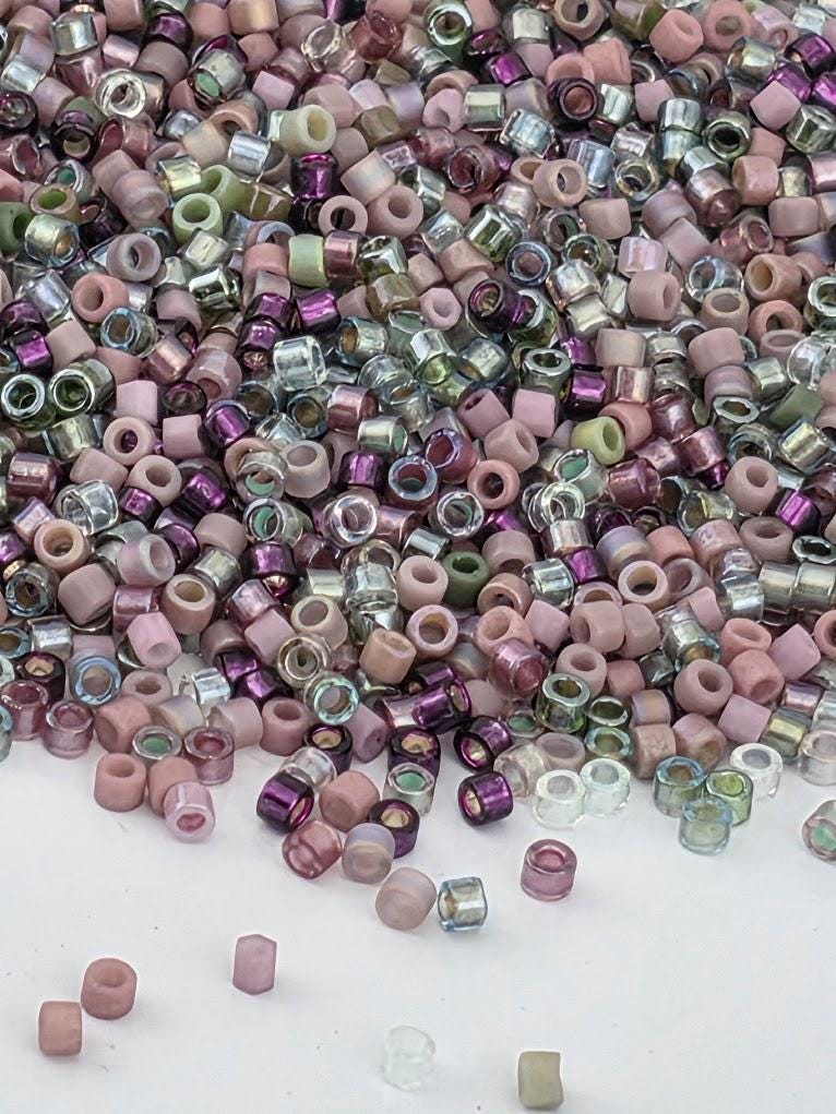 The image is a collection of various colored beads, including pink, purple, and green, scattered across a white surface.