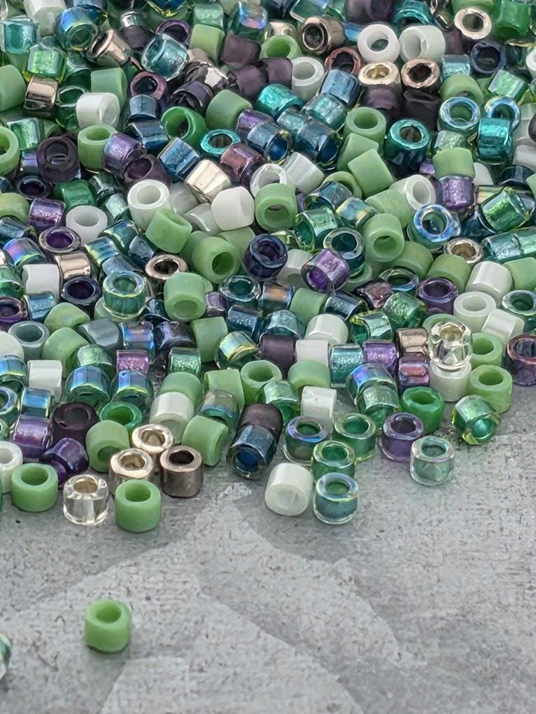 A pile of multicolored glass beads, including various shades of green, purple, and blue, scattered on a surface.