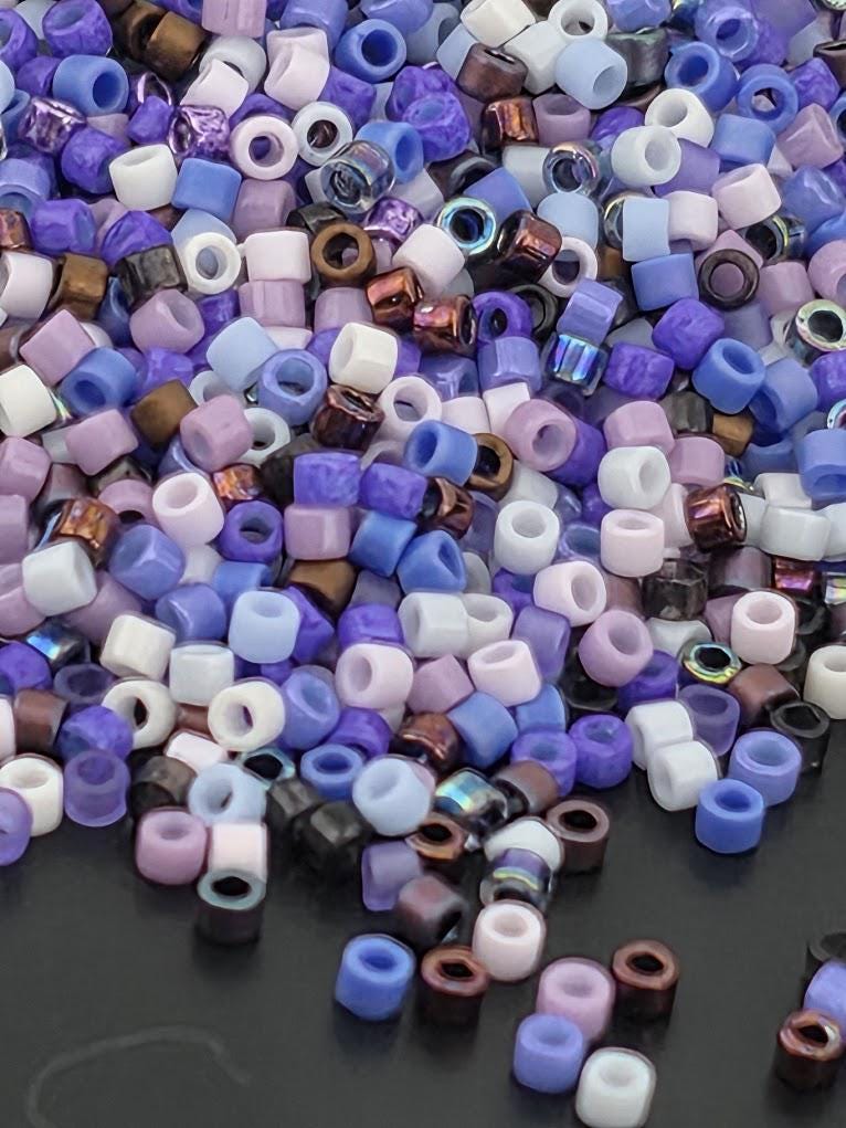 A pile of multicolored beads in various shades of purple, white, and brown, scattered on a dark surface.