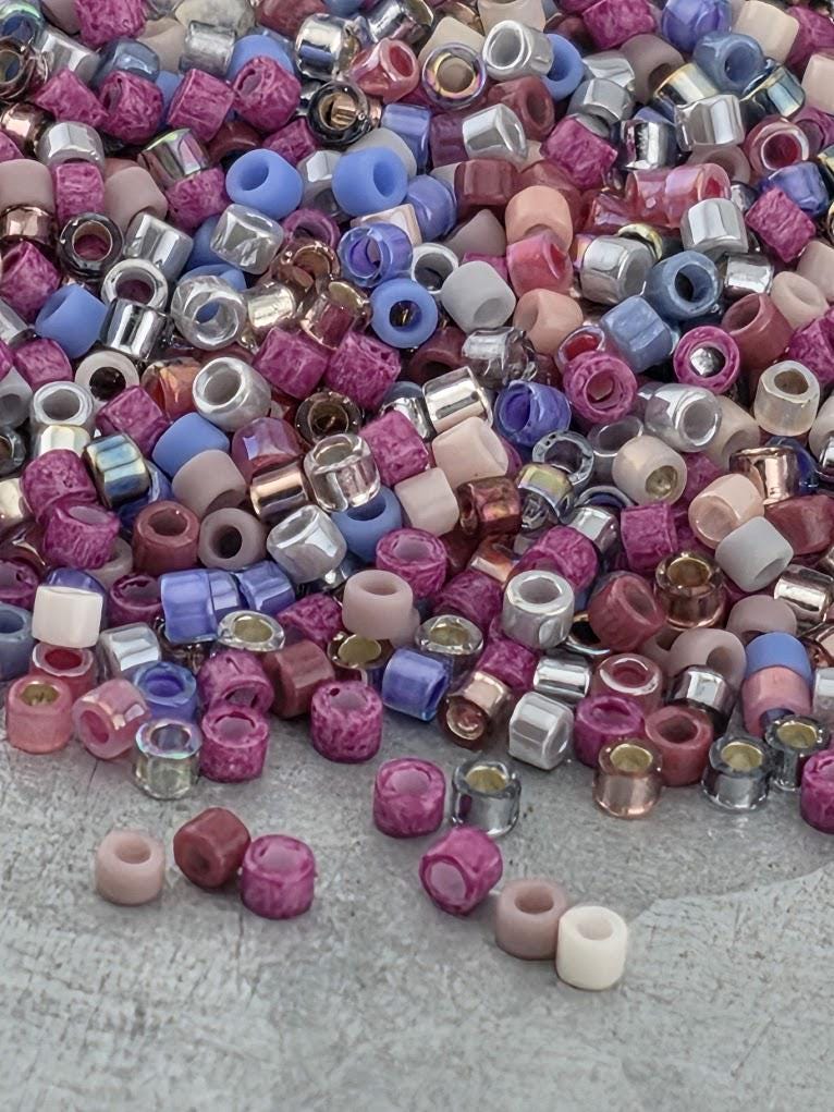A colorful pile of multicolored beads, including various shades of pink, purple, blue, and silver, scattered on a surface.