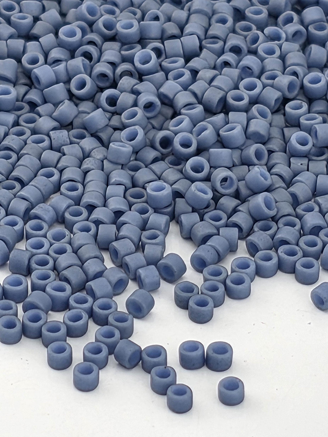 a close-up view of numerous small, round beads in various shades of blue, scattered across a white surface.
