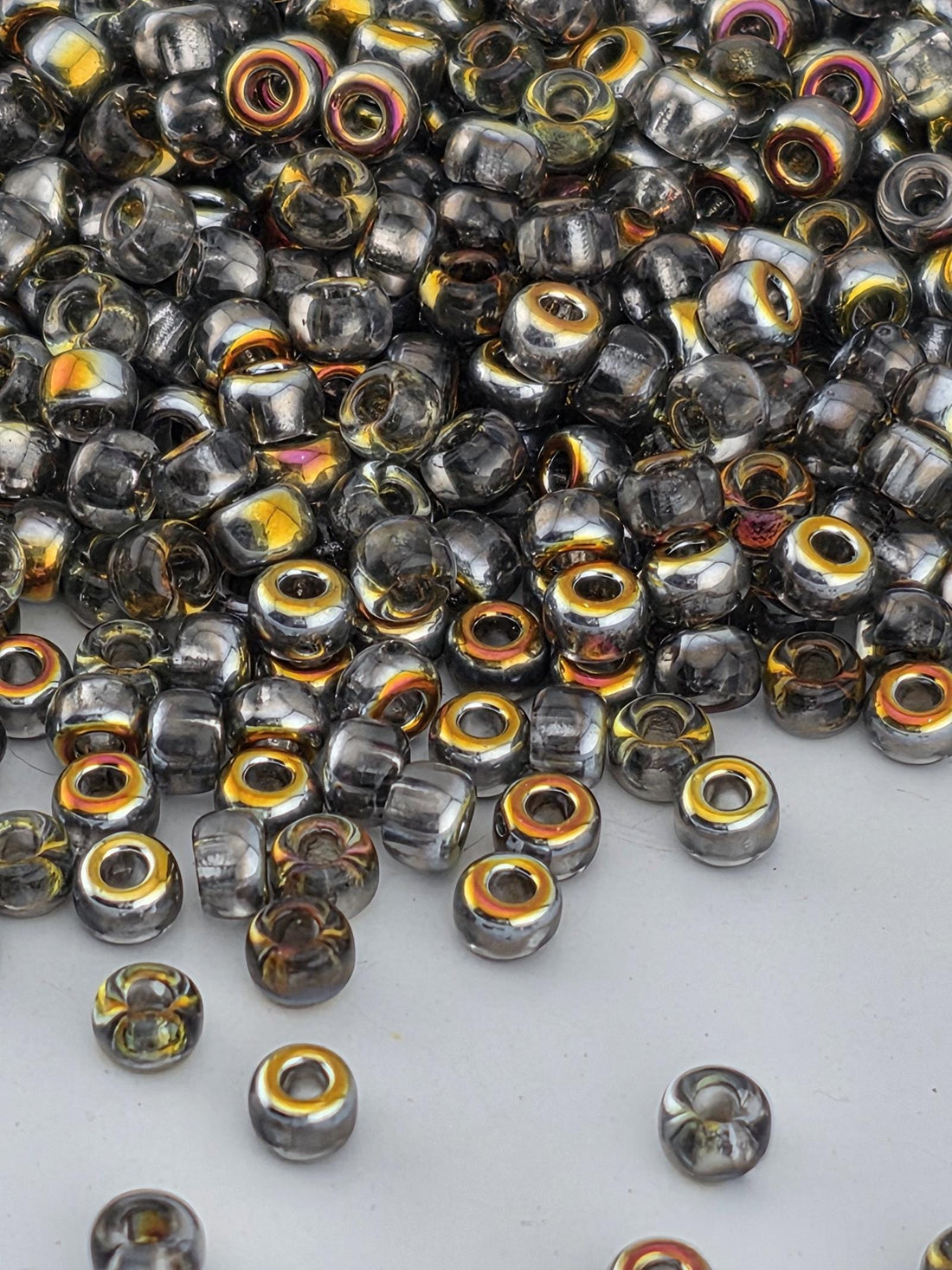 a close-up view of a pile of glass beads with a mix of silver and gold colors. The beads are scattered across a white surface, creating a visually striking contrast.