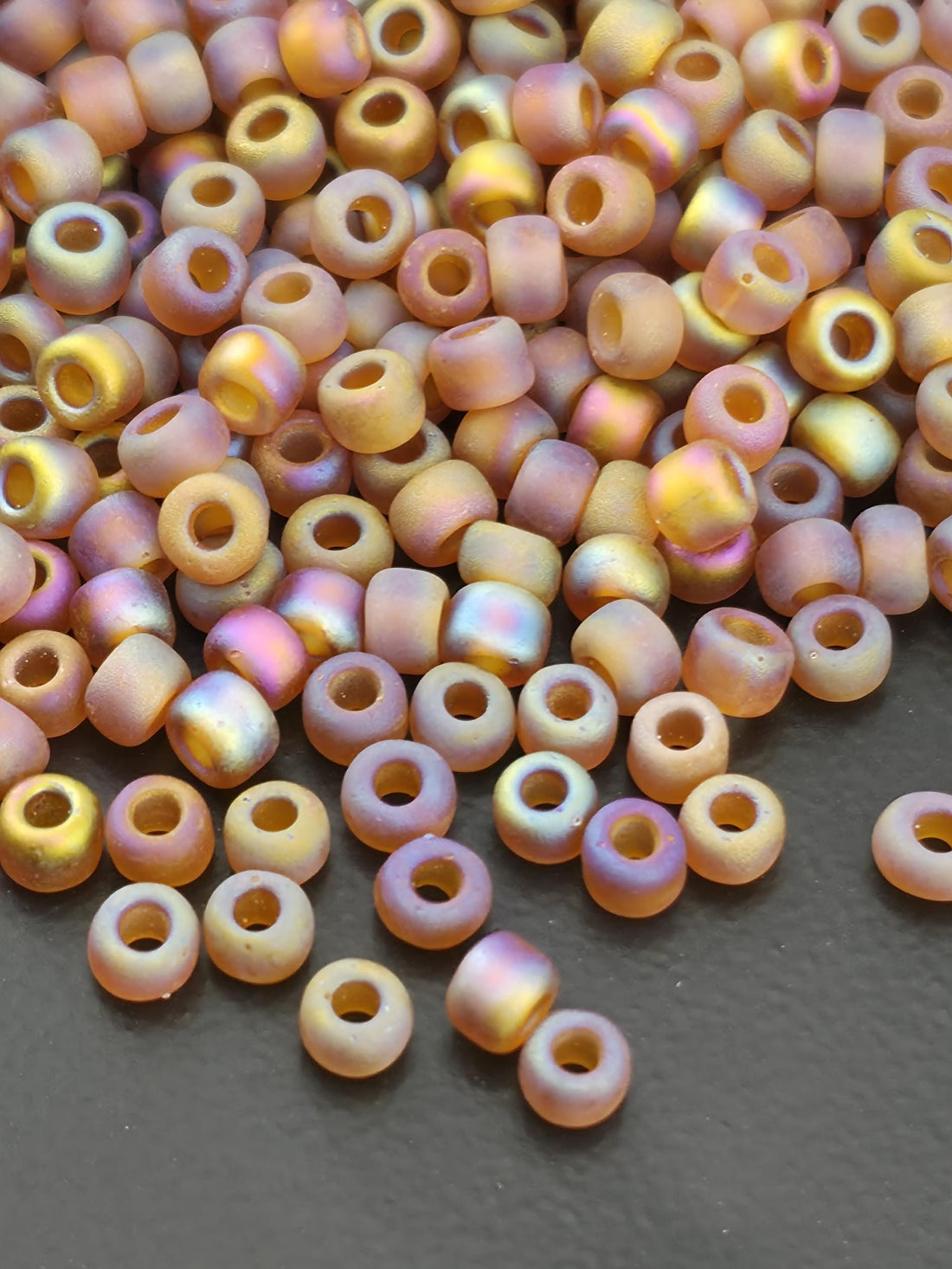 A close-up image of numerous multicolored beads scattered on a dark surface.