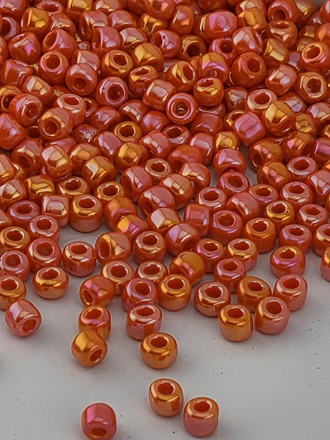 a large pile of small, round beads in various shades of orange and red, scattered on a white surface.