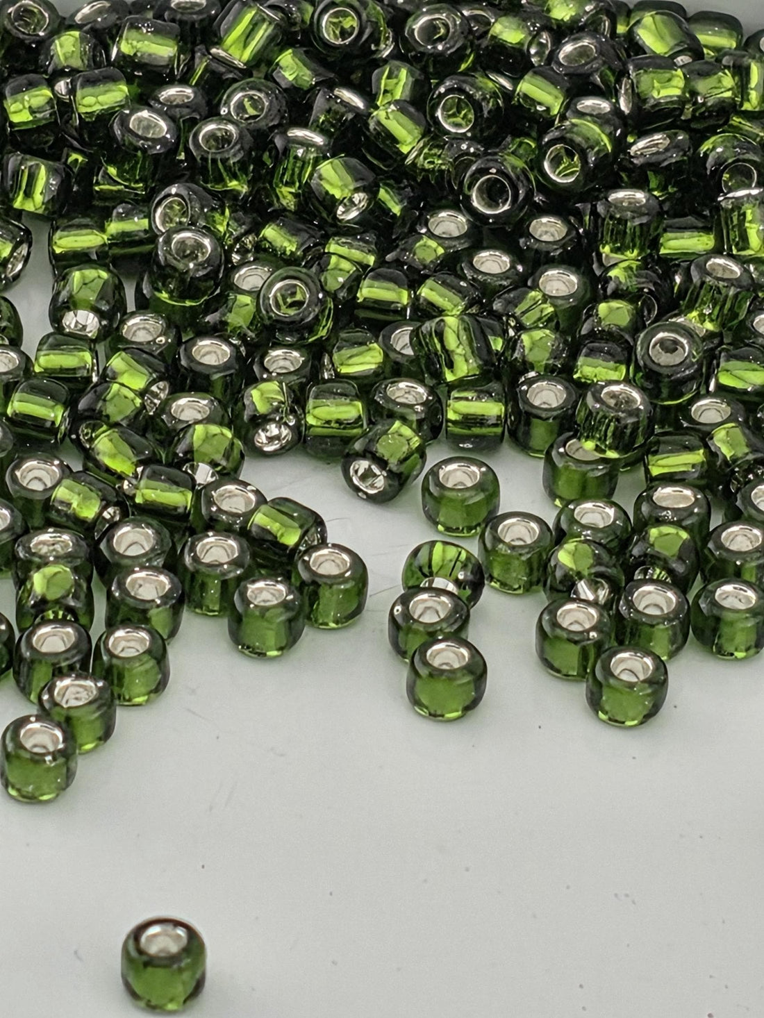 a large pile of green glass beads scattered on a white surface.