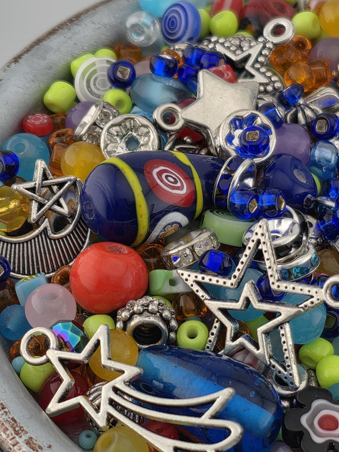 A colorful assortment of beads, charms, and other decorative items are scattered together in a bowl or container.