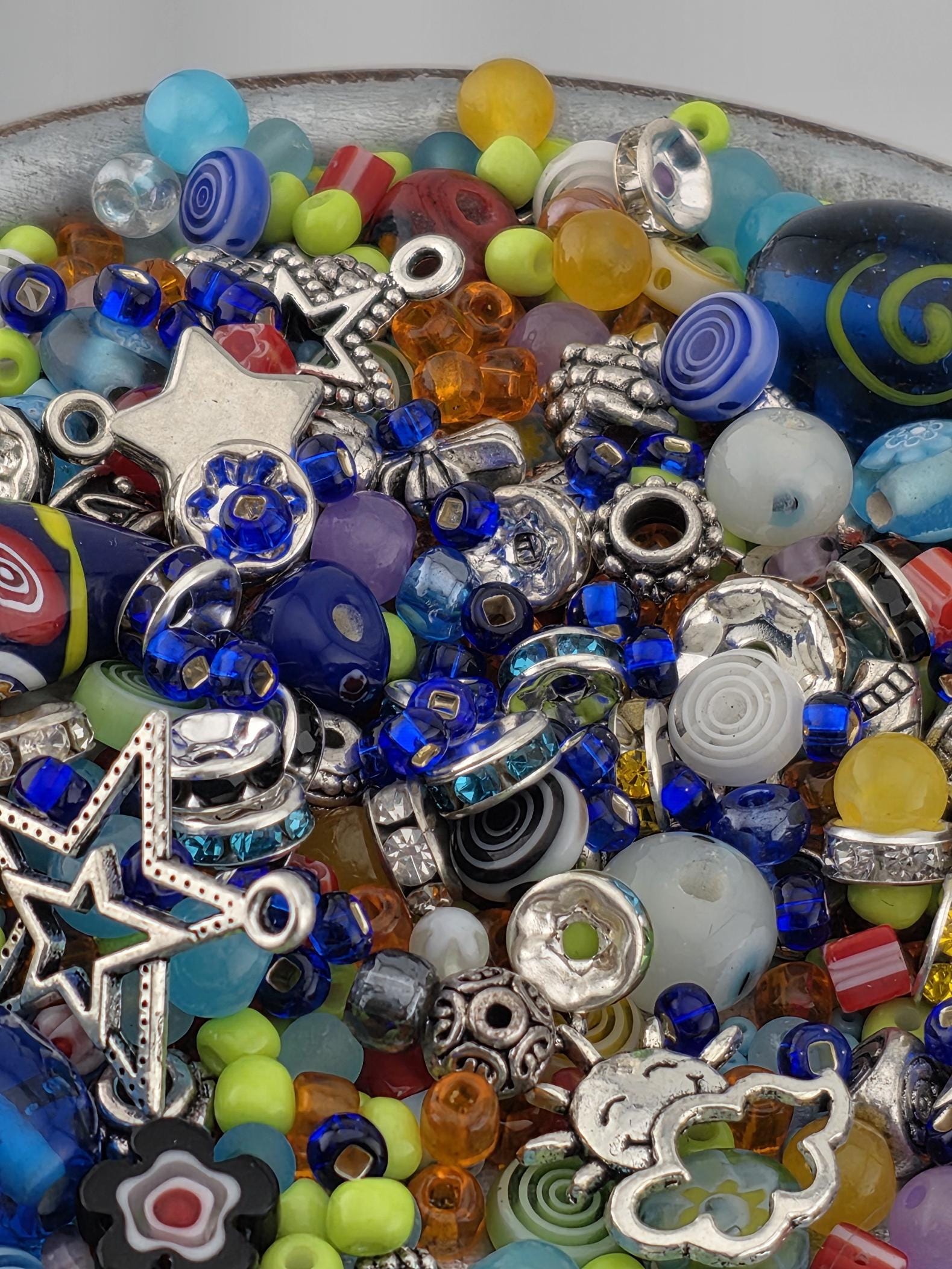 A colorful assortment of beads, charms, and other decorative items, including beads in various colors, metal charms, and other embellishments, all piled together.