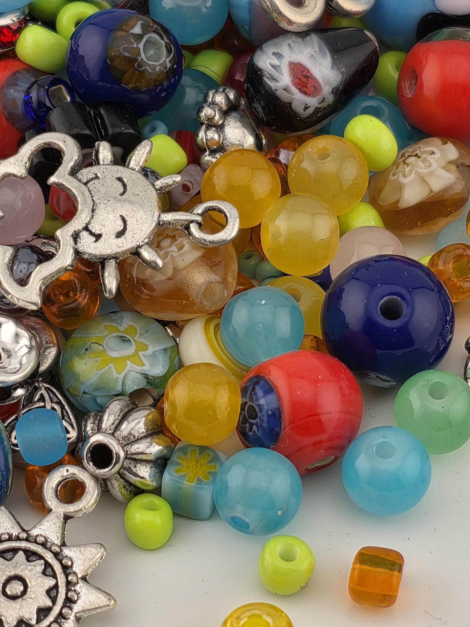 A colorful assortment of beads, charms, and other decorative items, including glass beads, metal charms, and other small objects, are scattered across the image.