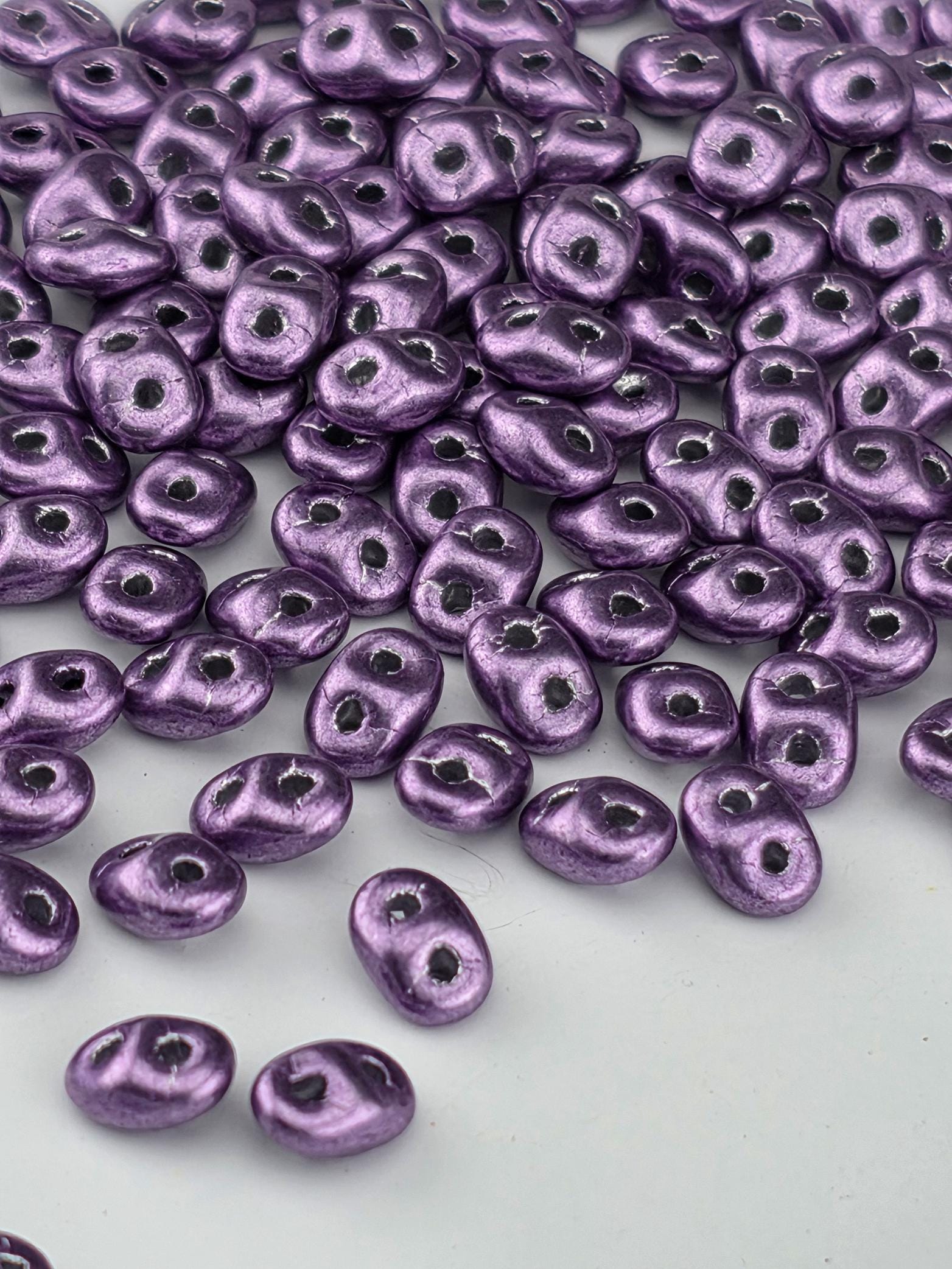 a close-up view of numerous small, shiny purple beads scattered across a white background.