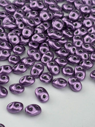 a close-up view of numerous small, shiny purple beads scattered across a white background.