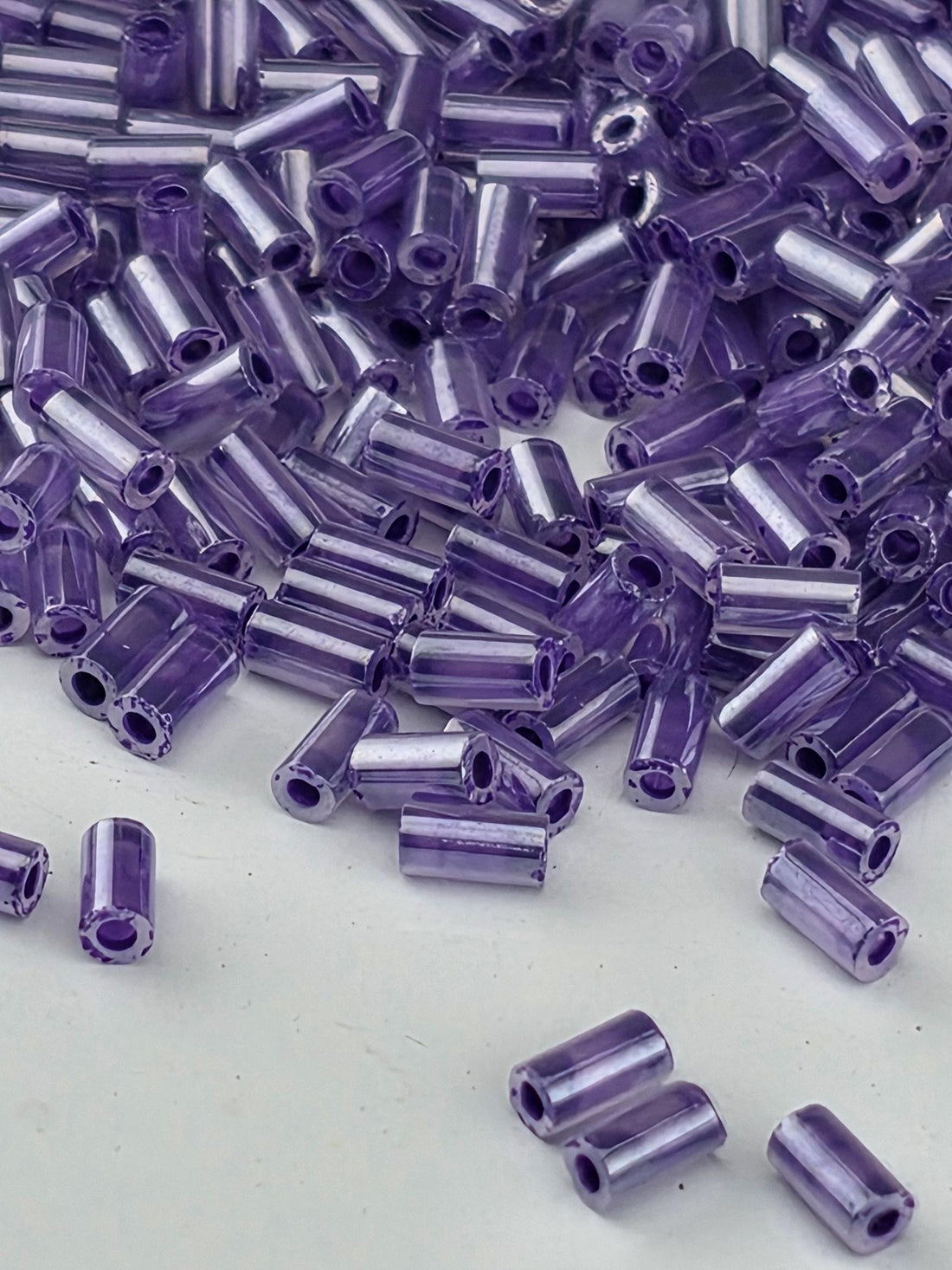 a close-up view of numerous small, clear beads in various shades of purple, scattered across a white surface.