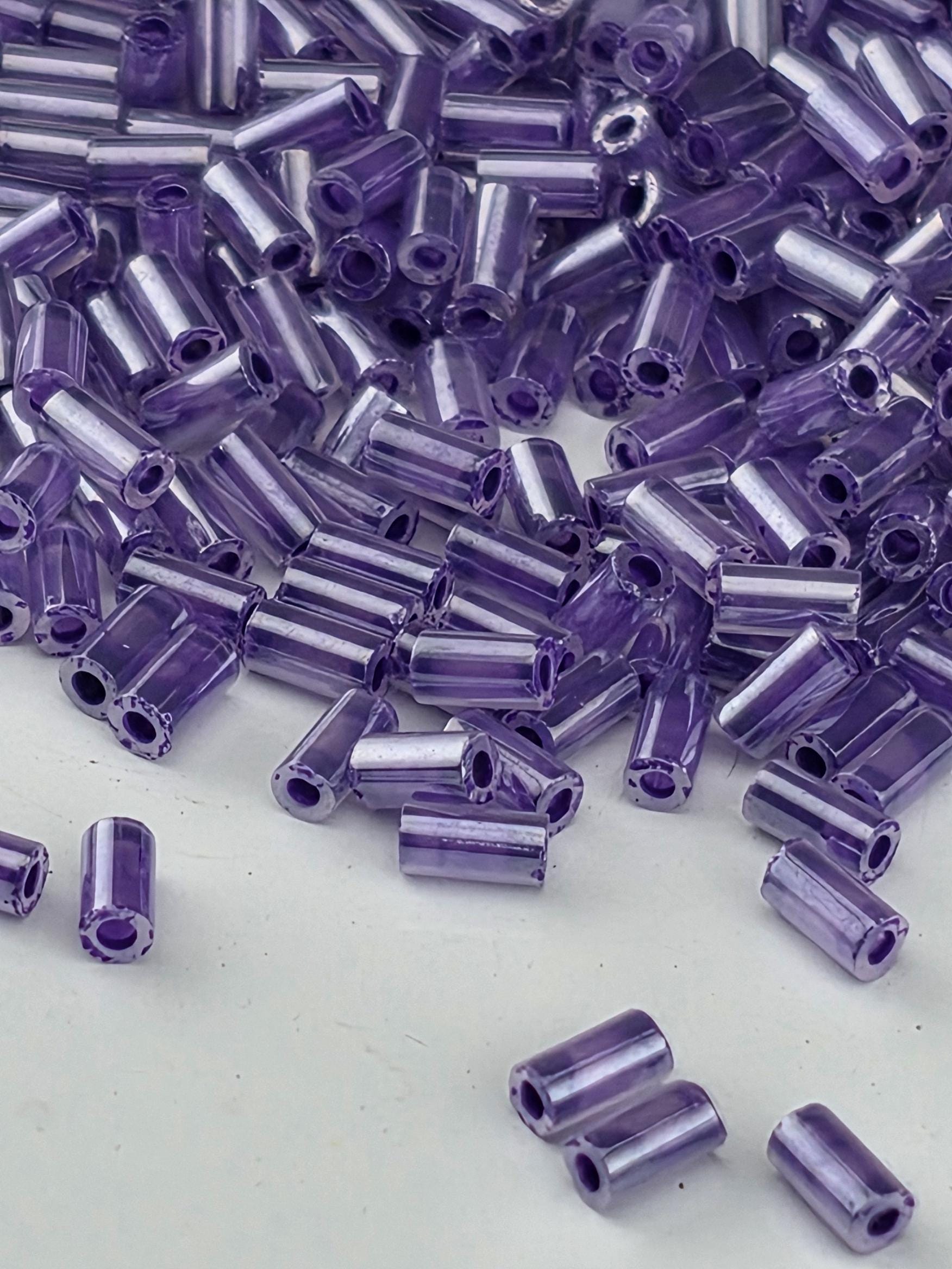 a close-up view of numerous small, clear beads in a variety of purple colors scattered across a white surface.