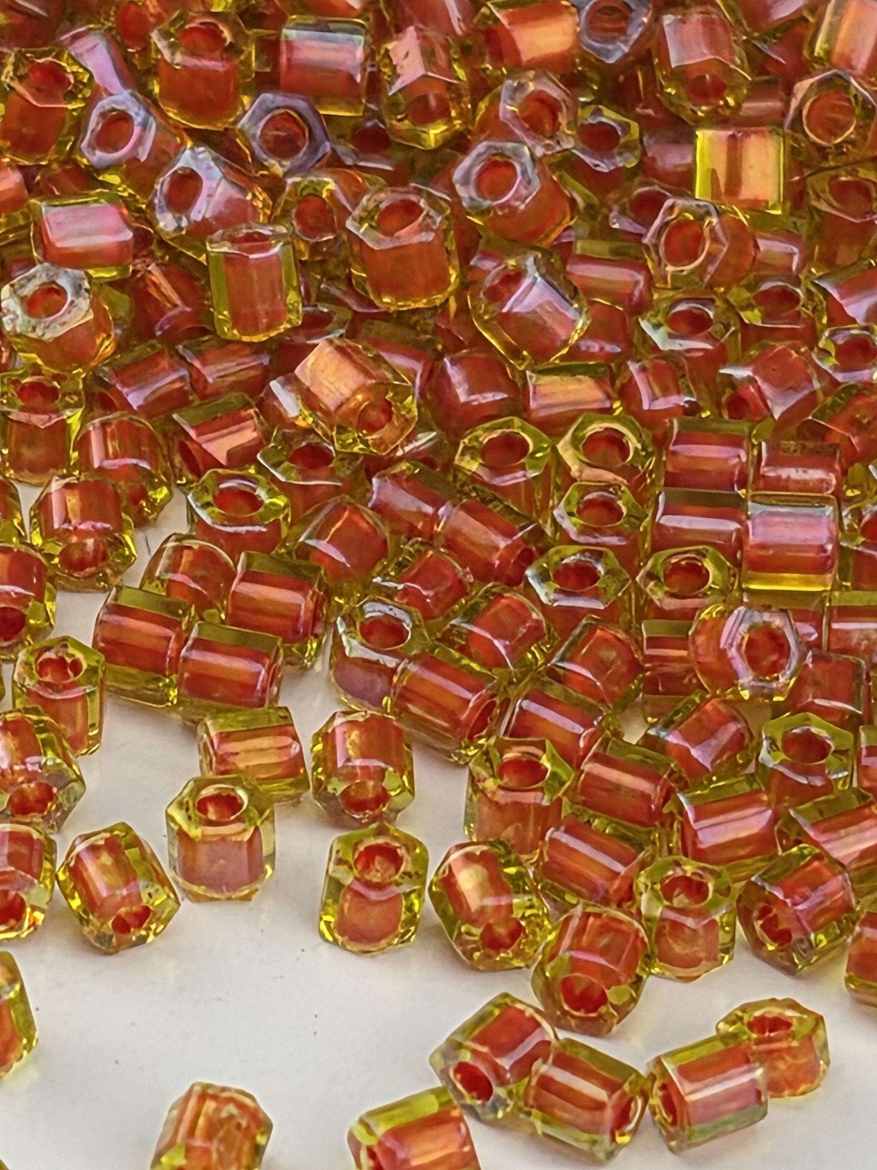 The image is a close-up of numerous small, colorful beads in shades of red and yellow, scattered across a surface.