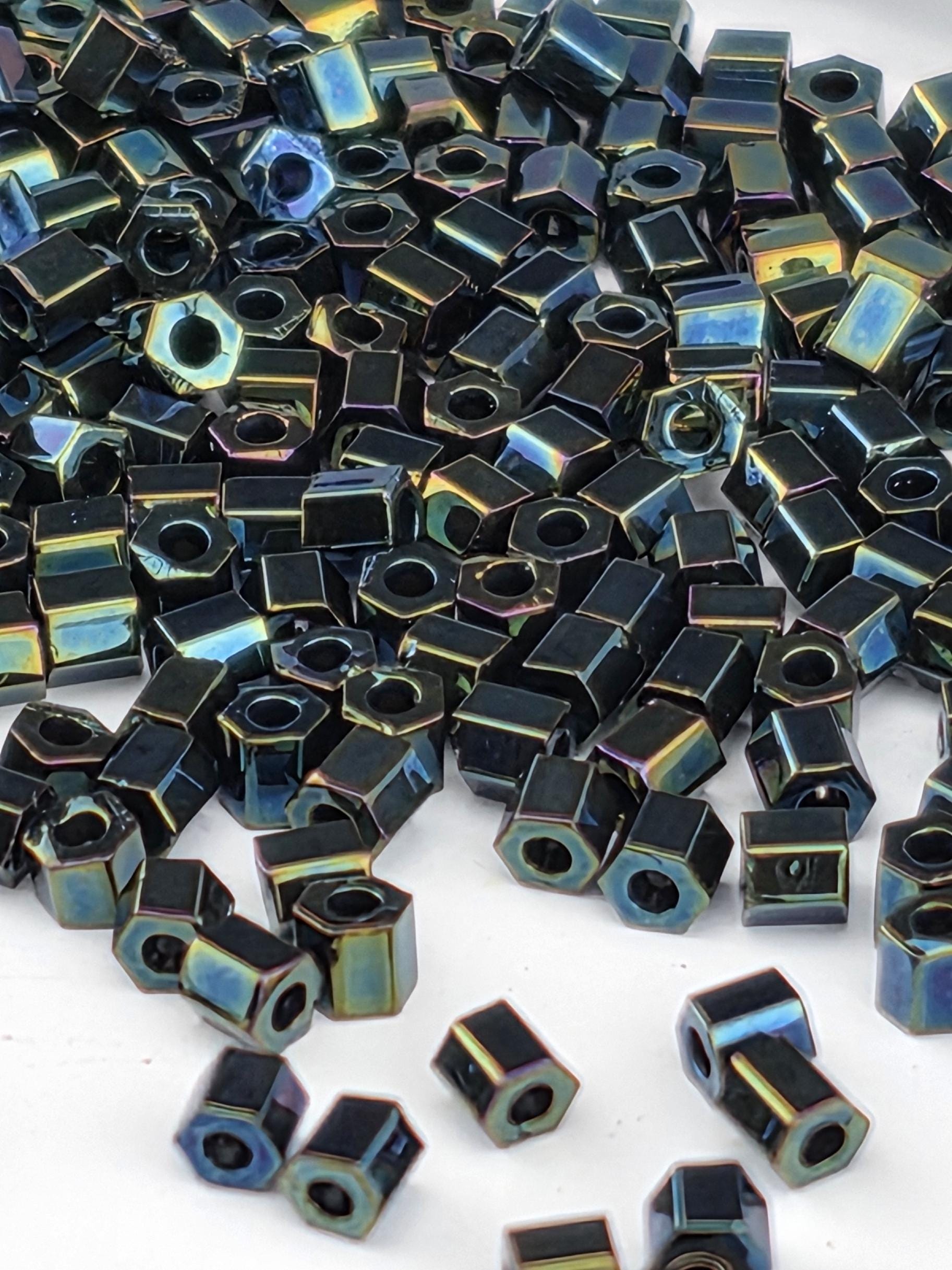 The image is a close-up of numerous black hexagonal beads or nuts scattered on a white surface.
