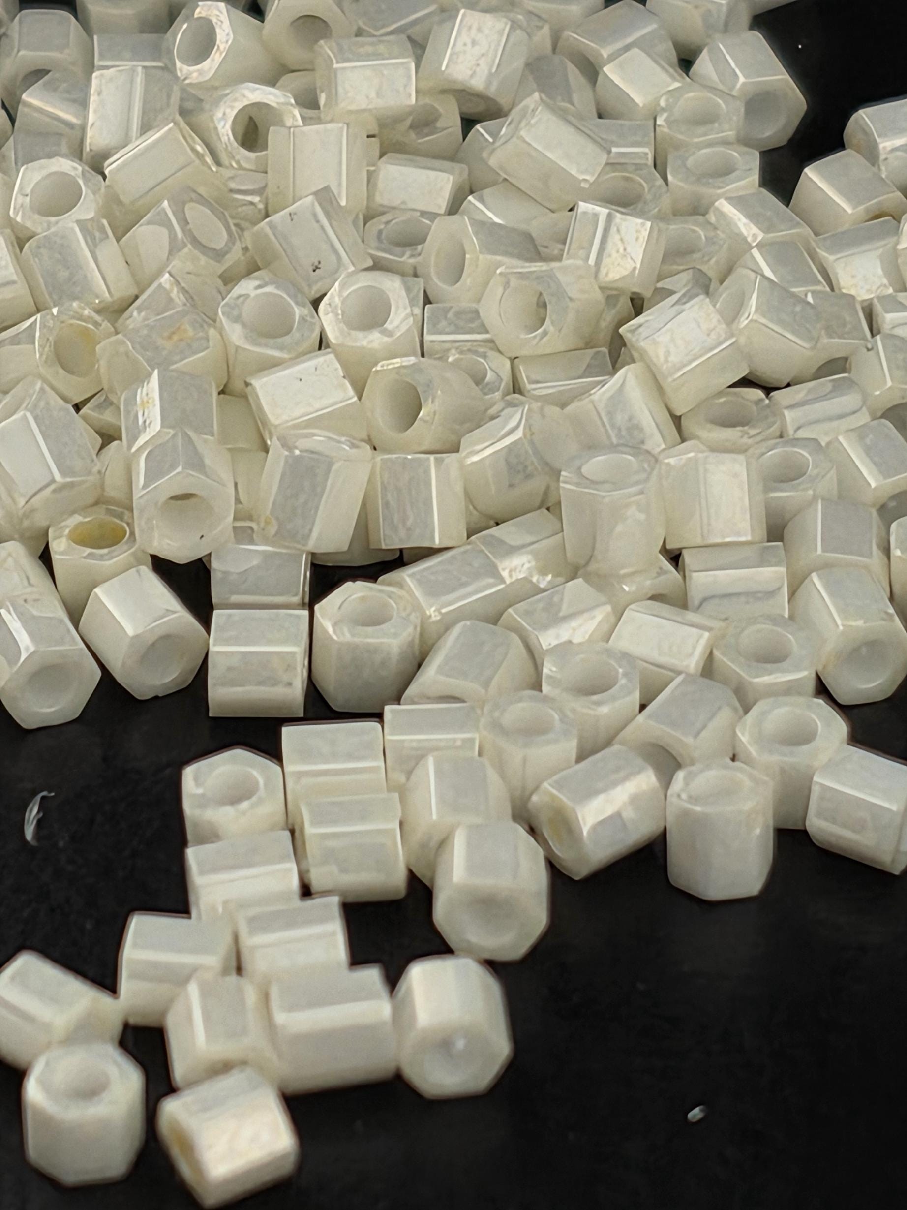 a pile of small white hexagonal objects, possibly beads or nuts, scattered on a dark background.
