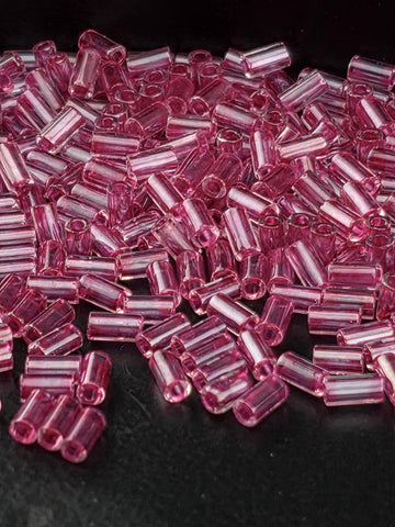 A close-up image of numerous small, clear beads in a vibrant shade of pink, scattered across a dark background.