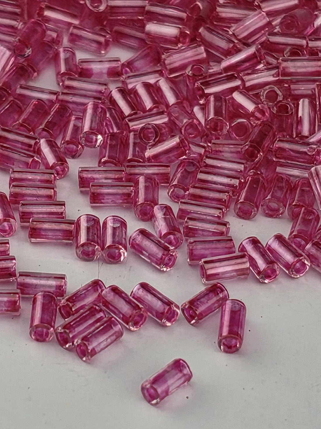 A close-up image of numerous small, clear beads in a vibrant shade of pink, scattered across a dark background.