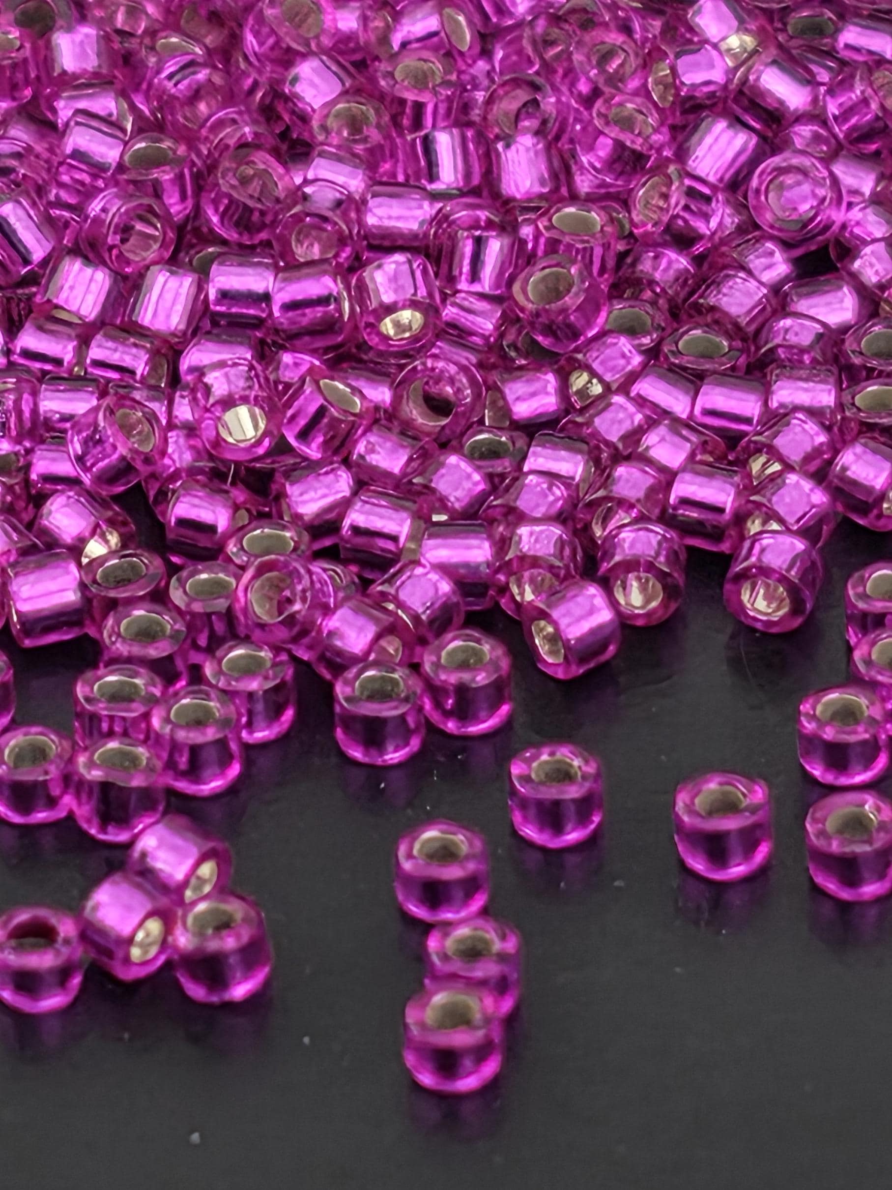 a close-up view of numerous small, clear beads in a vibrant shade of purple. The beads are scattered across a dark background, creating a visually striking contrast.