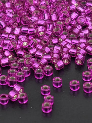 a close-up view of numerous small, clear beads in a vibrant shade of purple. The beads are scattered across a dark background, creating a visually striking contrast.