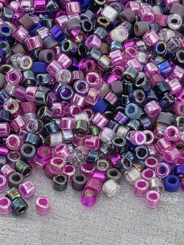 A colorful pile of multicolored beads, including shades of pink, purple, blue, and black, scattered across a surface.