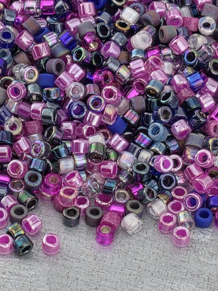 A colorful pile of multicolored beads, including shades of pink, purple, blue, and black, scattered across a surface.
