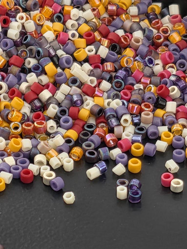 A colorful pile of multicolored beads, including red, yellow, purple, and white, scattered on a dark surface.